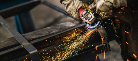 Heavy industry worker grinds steel with an angle grinder,sparks flying,close up.